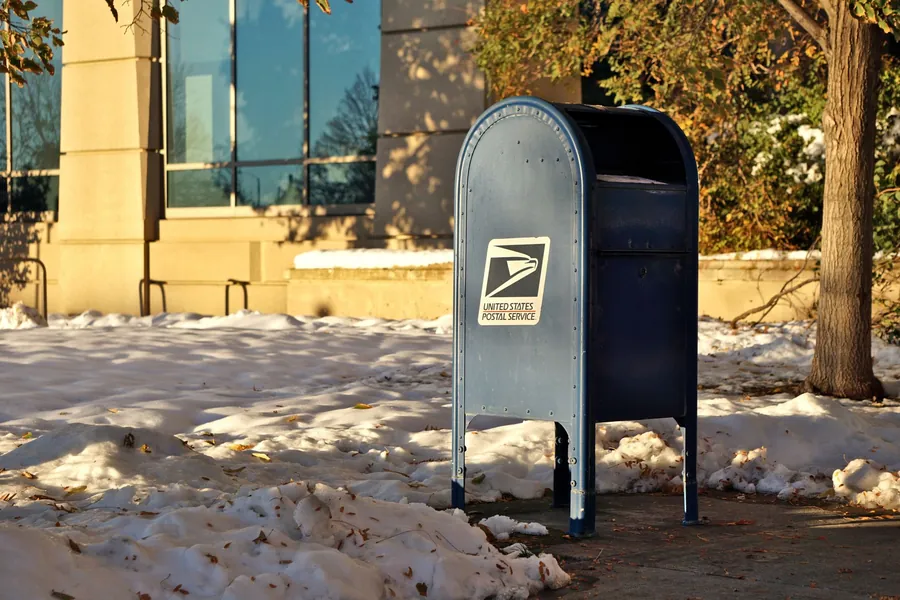 A blue postal mailbox on a street corner in low winter sunlight.