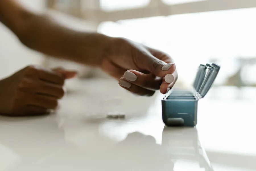 A hand filling a weekly pill organizer on a kitchen table.